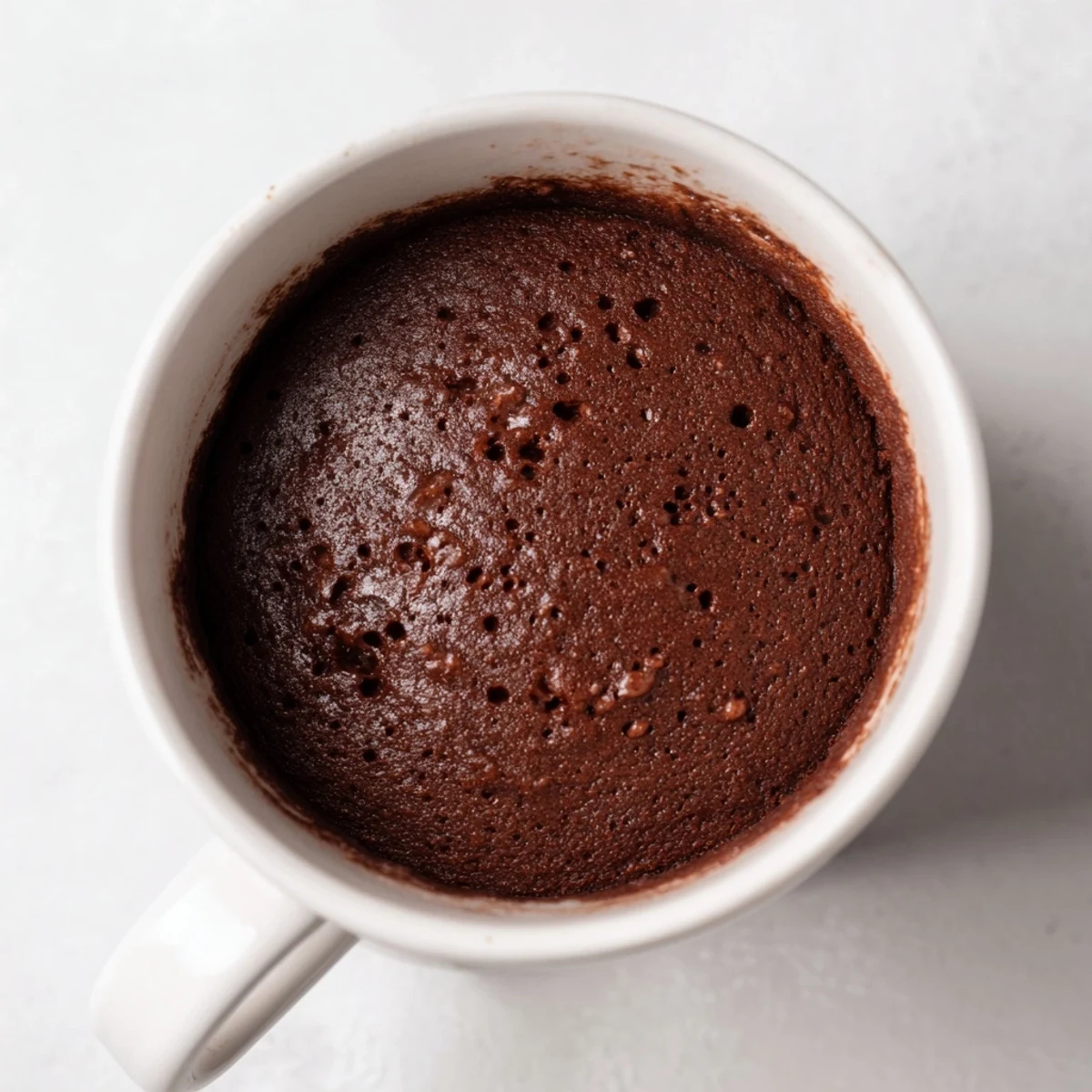 A close-up shot of a fluffy, warm microwave mug cake topped with whipped cream.