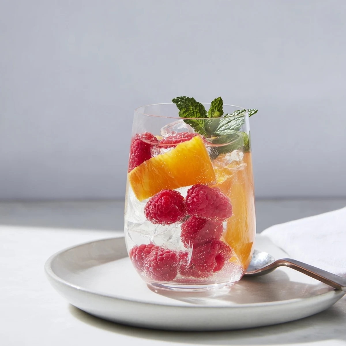 Vibrant sparkling juice with raspberries, adorned with orange slices and mint, ready to enjoy.