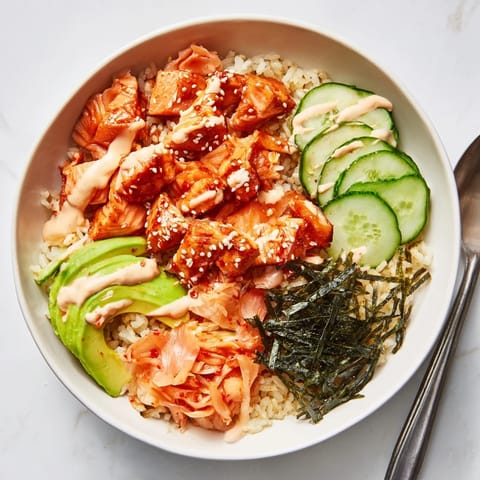 Flavorful crispy salmon rice bowl garnished with garlic, cucumber, and toasted sesame seeds.  