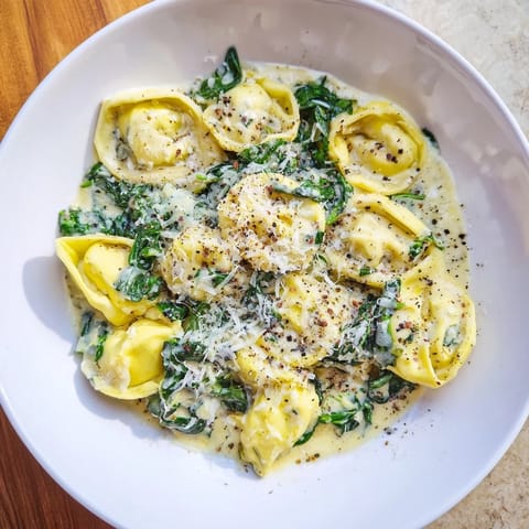 A close-up of creamy spinach Alfredo tortellini, showing the rich Alfredo sauce clinging to the pasta.