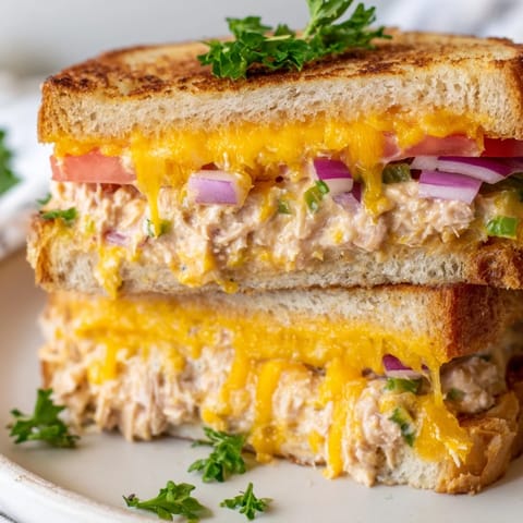 Fresh red onion and celery flecks peek through the bright orange melted cheese in a close-up of a hearty Spicy Tuna Melt.  