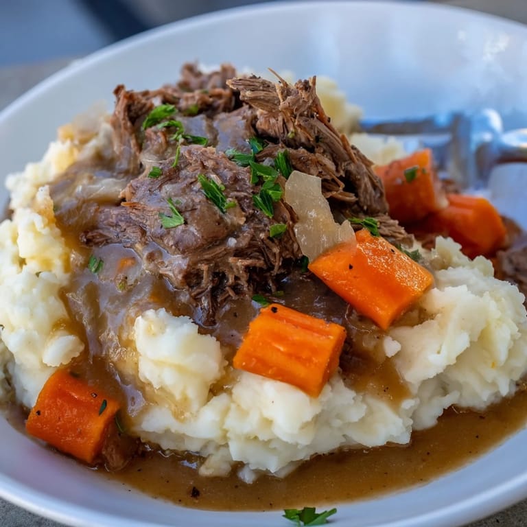 Tender beef roast drenched in rich gravy, resting on creamy mashed potatoes.