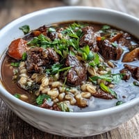 Hearty One-Pot Guinness Beef and Barley Stew with tender beef, root vegetables, and rich stout broth simmering in a Dutch oven.  